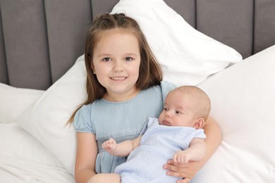 Photo of Cute girl and her little sister on bed at home
