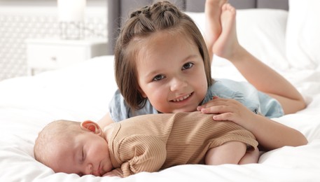 Photo of Cute girl and her little sister on bed at home