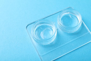 Photo of Contact lenses in case on light blue background, closeup