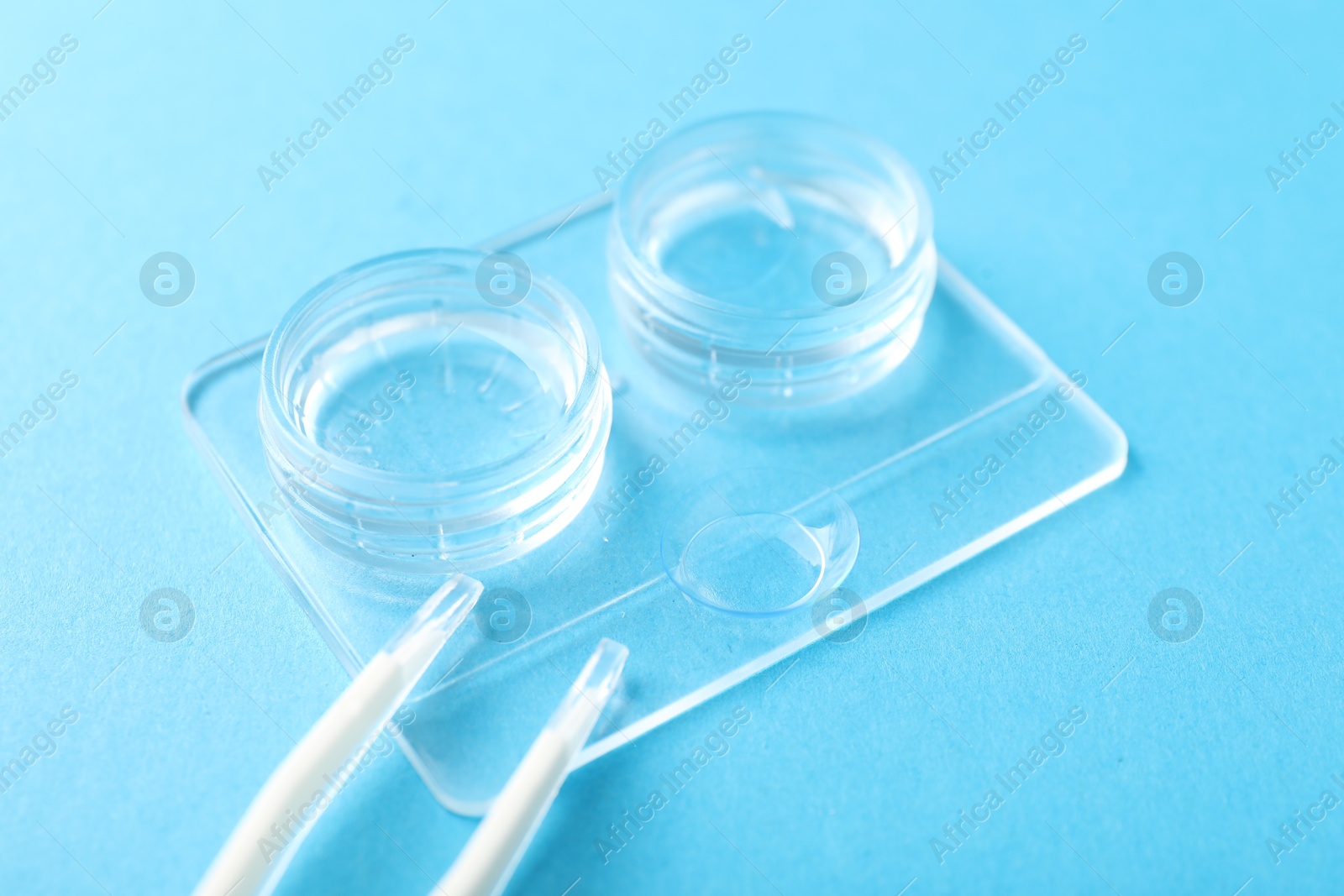 Contact lenses, case and tweezers on light blue background, closeup Photo of Contact lenses, case and tweezers on light blue background, closeup