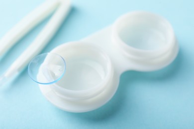 Photo of Contact lenses, case and tweezers on light blue background, closeup
