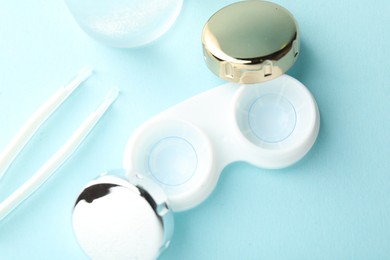 Photo of Contact lenses in case and tweezers on light turquoise background, flat lay