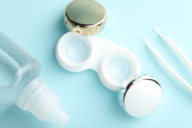 Photo of Contact lenses in case, solution and tweezers on light turquoise background, flat lay