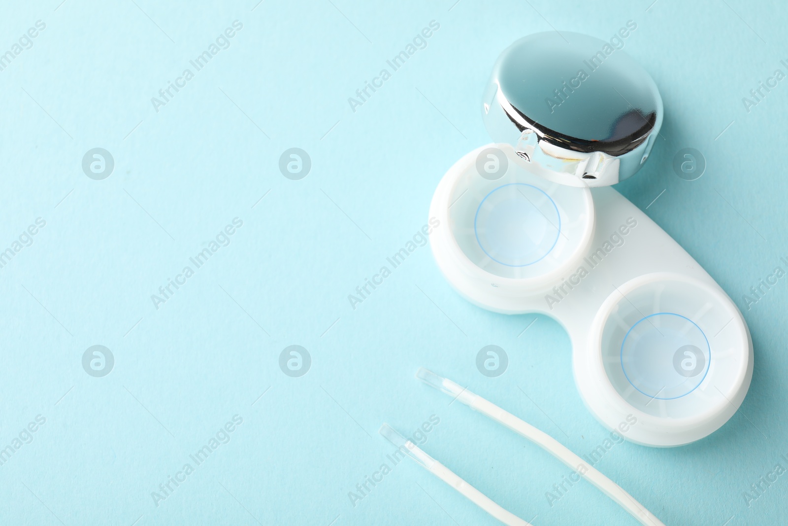Contact lenses in case and tweezers on light turquoise background, flat lay. Space for text Photo of Contact lenses in case and tweezers on light turquoise background, flat lay. Space for text