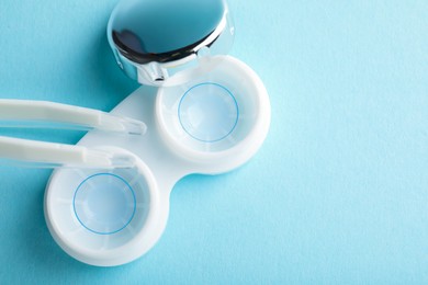 Photo of Contact lenses in case and tweezers on light blue background, flat lay. Space for text