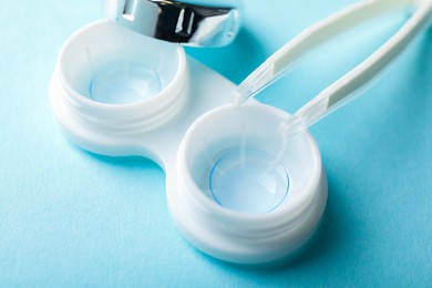 Photo of Contact lenses in case and tweezers on light blue background, closeup