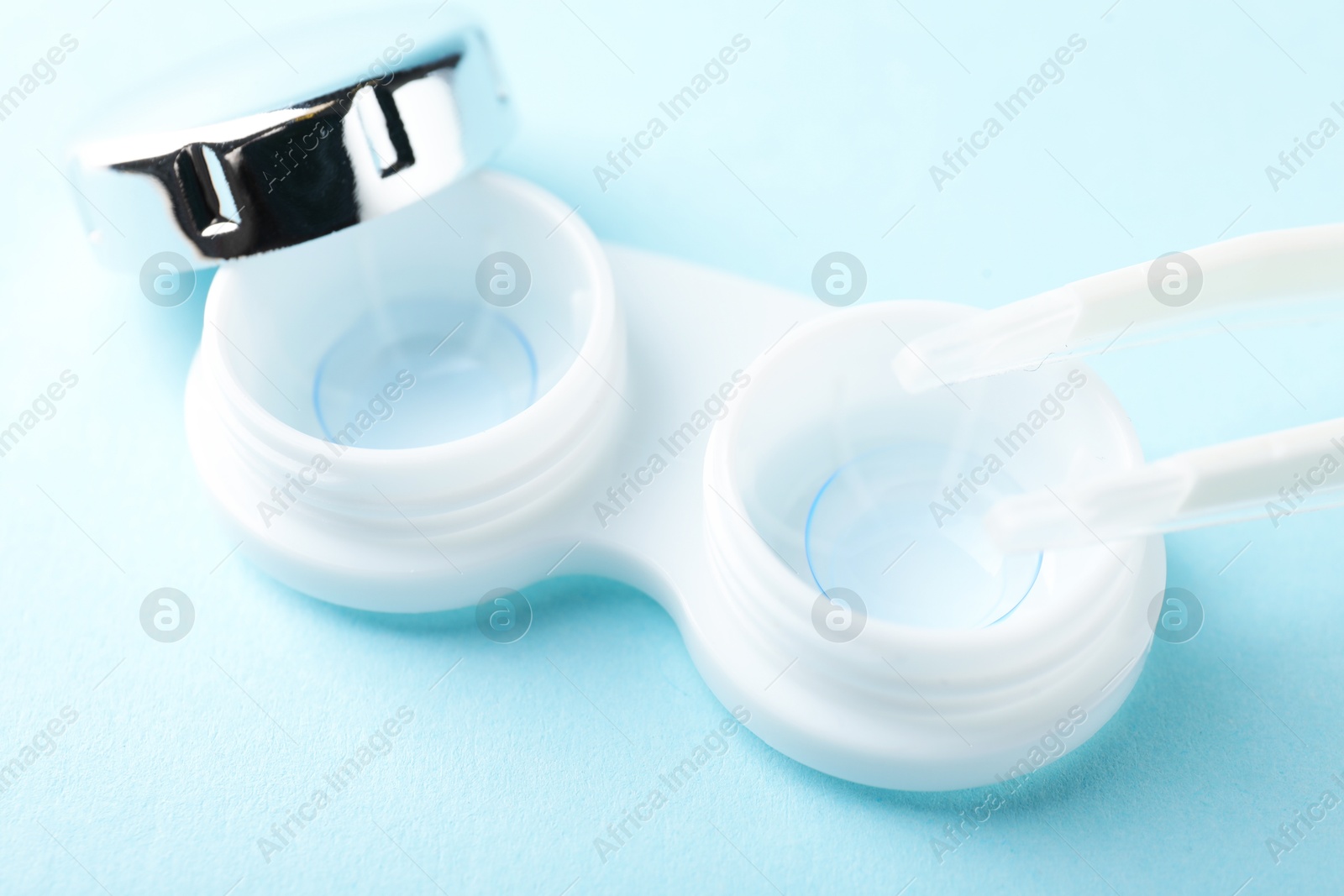 Contact lenses in case and tweezers on light blue background, closeup Photo of Contact lenses in case and tweezers on light blue background, closeup