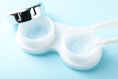 Photo of Contact lenses in case and tweezers on light blue background, closeup