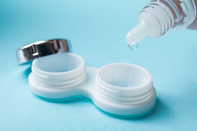 Photo of Dripping contact lens solution from bottle into case on light blue background, closeup