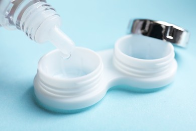 Photo of Dripping contact lens solution from bottle into case on light blue background, closeup