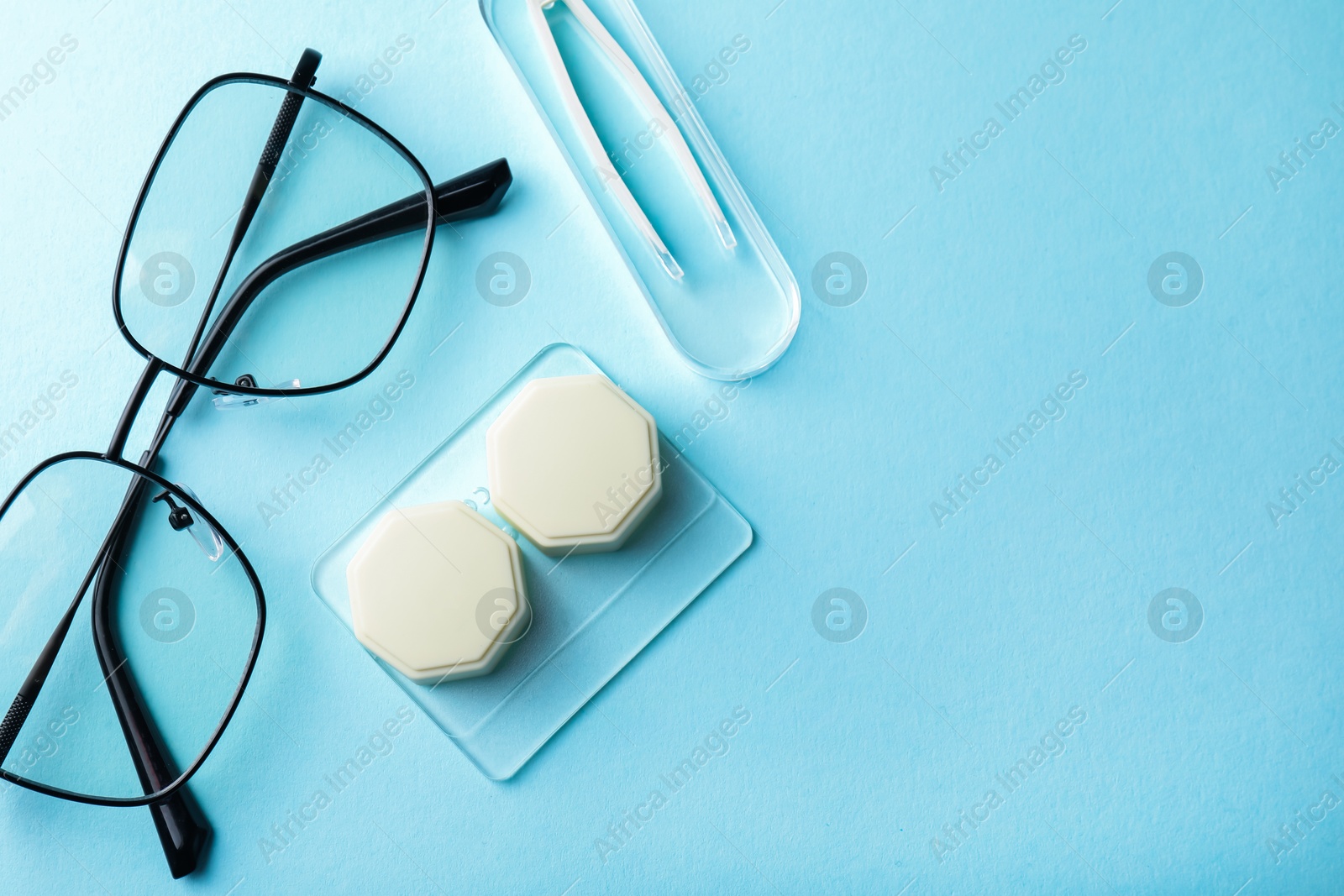 Contact lens case, glasses and tweezers on light blue background, flat lay. Space for text Photo of Contact lens case, glasses and tweezers on light blue background, flat lay. Space for text