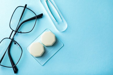 Photo of Contact lens case, glasses and tweezers on light blue background, flat lay. Space for text