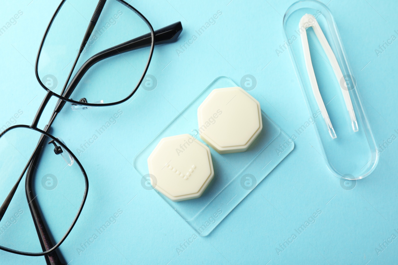 Contact lens case, glasses and tweezers on light turquoise background, flat lay Photo of Contact lens case, glasses and tweezers on light turquoise background, flat lay