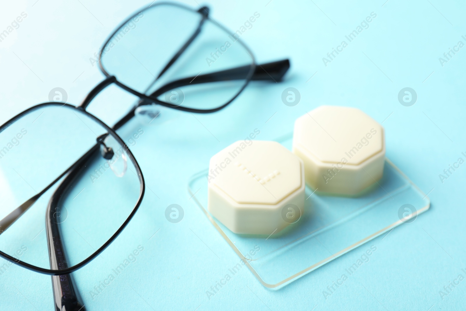 Contact lens case, glasses and tweezers on light turquoise background, closeup Photo of Contact lens case, glasses and tweezers on light turquoise background, closeup