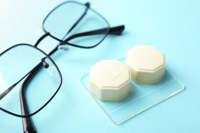Photo of Contact lens case, glasses and tweezers on light turquoise background, closeup