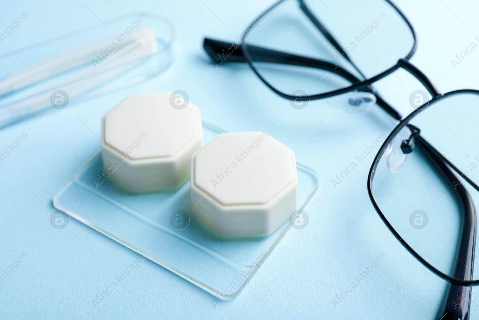 Contact lens case, glasses and tweezers on light blue background, closeup Photo of Contact lens case, glasses and tweezers on light blue background, closeup