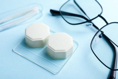 Photo of Contact lens case, glasses and tweezers on light blue background, closeup