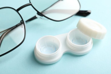 Photo of Contact lenses in case and glasses on light turquoise background, closeup