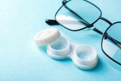 Photo of Contact lenses in case and glasses on light blue background, closeup