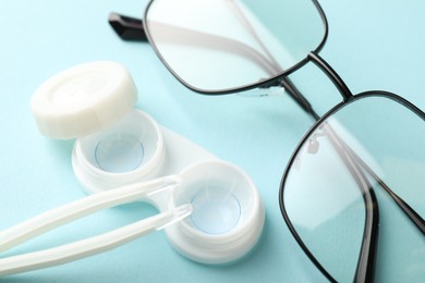 Photo of Contact lenses in case, tweezers and glasses on light turquoise background, closeup