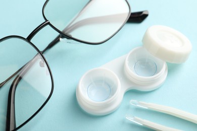 Photo of Contact lenses in case, tweezers and glasses on light turquoise background, above view