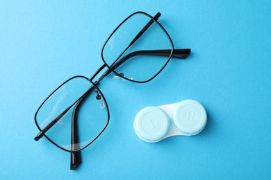 Photo of Contact lens case and glasses on light blue background, flat lay
