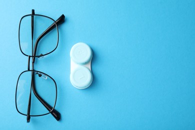 Photo of Contact lens case and glasses on light blue background, flat lay. Space for text