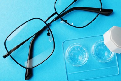 Photo of Contact lenses in case and glasses on light blue background, flat lay