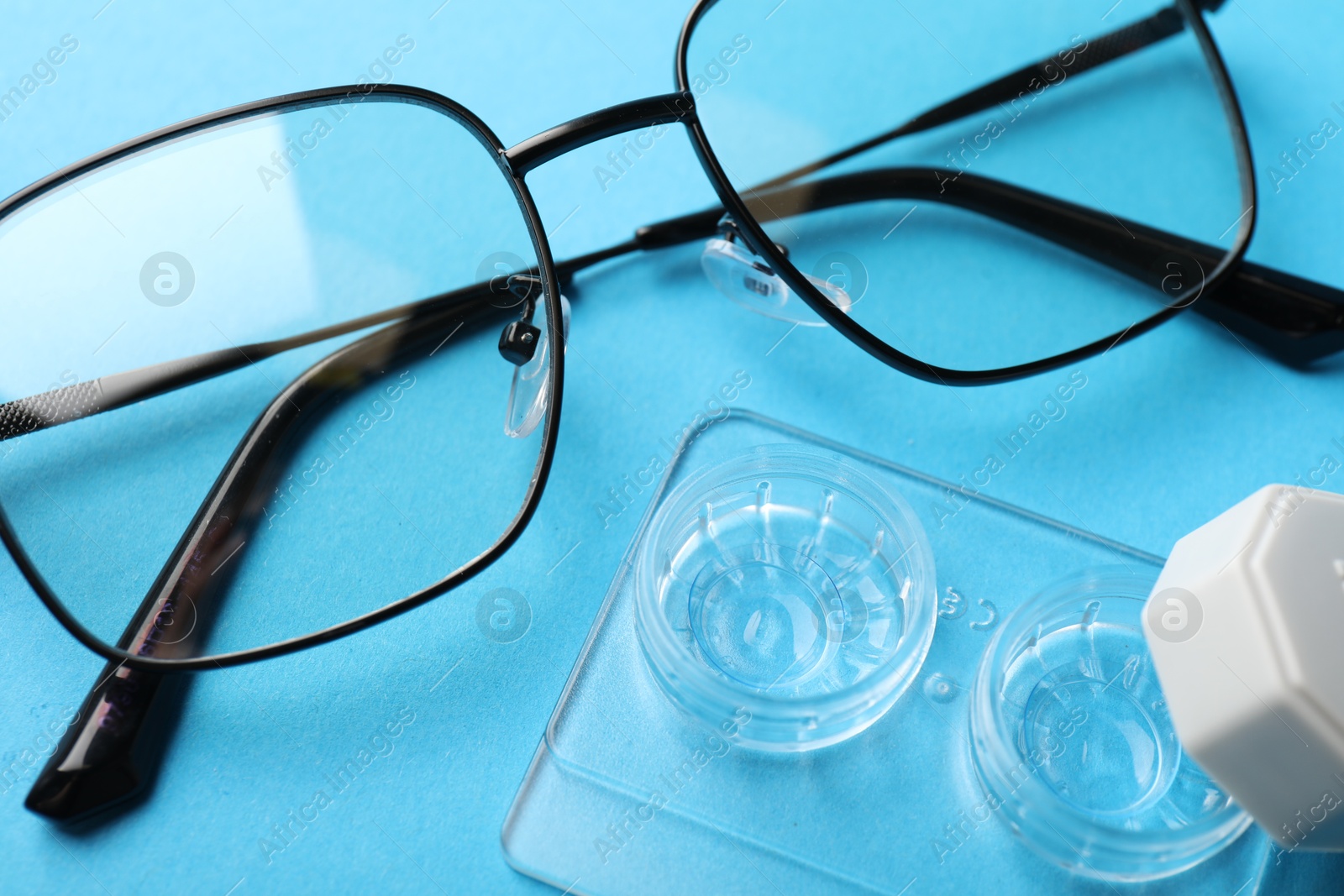 Contact lenses in case and glasses on light blue background, above view Photo of Contact lenses in case and glasses on light blue background, above view