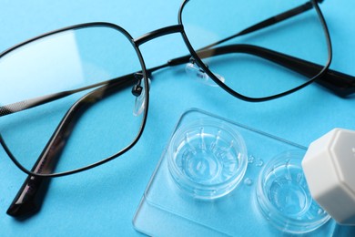 Photo of Contact lenses in case and glasses on light blue background, above view