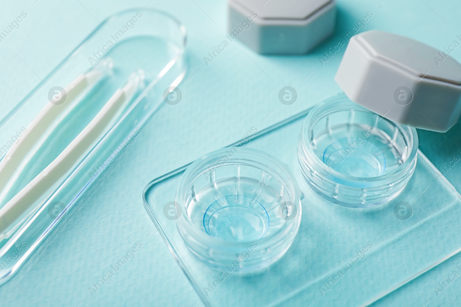 Contact lenses in case and tweezers on light turquoise background, closeup Photo of Contact lenses in case and tweezers on light turquoise background, closeup