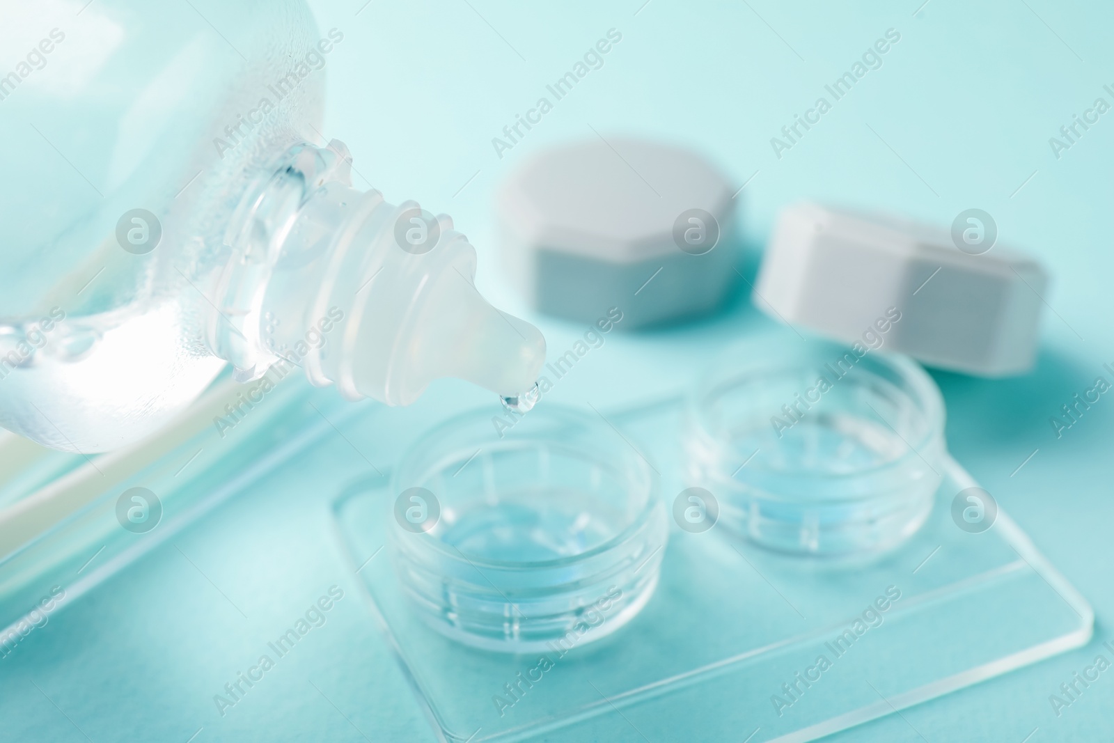 Dripping contact lens solution from bottle into case on light turquoise background, closeup Photo of Dripping contact lens solution from bottle into case on light turquoise background, closeup