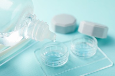 Photo of Dripping contact lens solution from bottle into case on light turquoise background, closeup