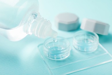 Photo of Dripping contact lens solution from bottle into case on light turquoise background, closeup
