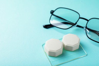 Photo of Contact lens case and glasses on turquoise background, closeup. Space for text