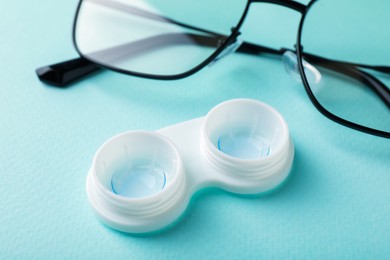 Photo of Contact lenses in case and glasses on turquoise background, closeup