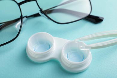 Photo of Contact lenses in case, tweezers and glasses on turquoise background, closeup