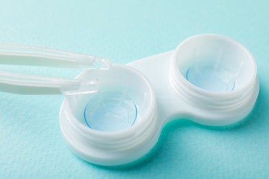 Photo of Contact lenses in case and tweezers on turquoise background, closeup