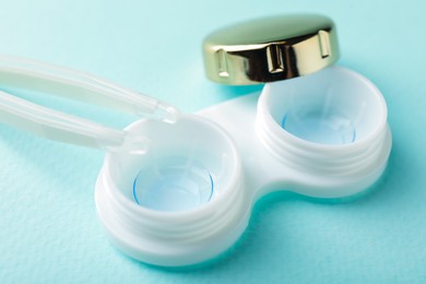 Photo of Contact lenses in case and tweezers on turquoise background, closeup