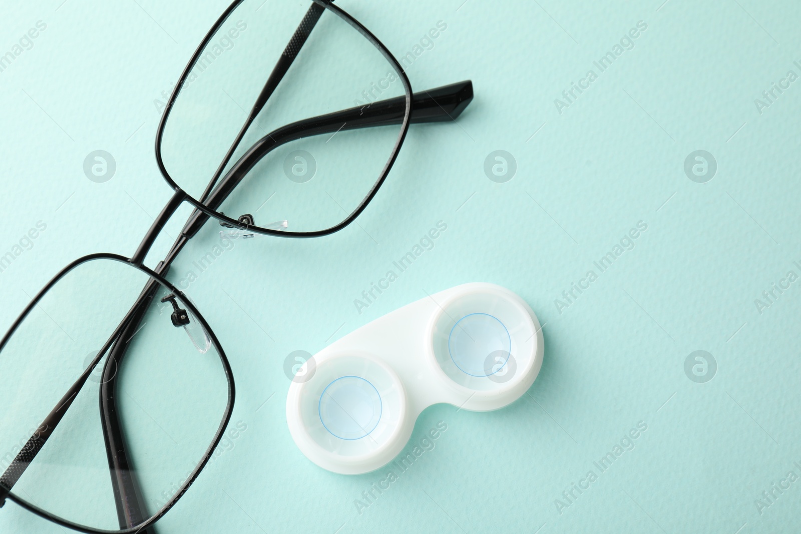 Contact lenses in case and glasses on light turquoise background, flat lay Photo of Contact lenses in case and glasses on light turquoise background, flat lay