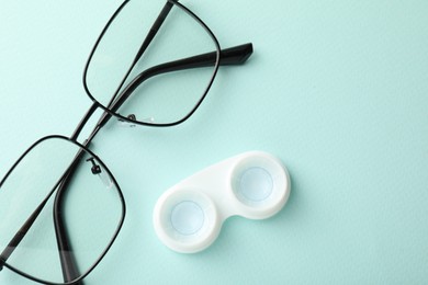 Photo of Contact lenses in case and glasses on light turquoise background, flat lay