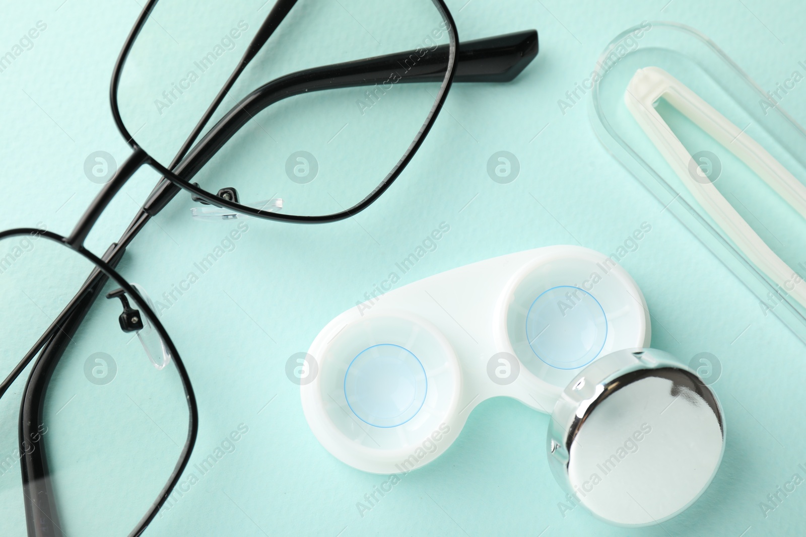 Contact lenses in case, tweezers and glasses on light turquoise background, flat lay Photo of Contact lenses in case, tweezers and glasses on light turquoise background, flat lay
