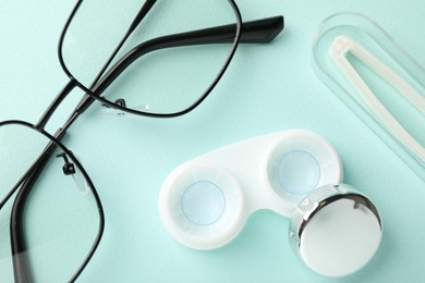 Photo of Contact lenses in case, tweezers and glasses on light turquoise background, flat lay