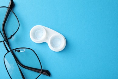 Photo of Contact lenses in case and glasses on blue background, flat lay. Space for text