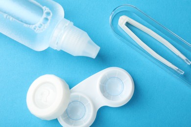 Photo of Contact lenses in case, solution and tweezers on blue background, flat lay