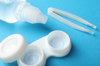 Photo of Contact lenses in case, solution and tweezers on blue background, closeup