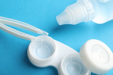 Photo of Contact lenses in case, solution and tweezers on blue background, above view