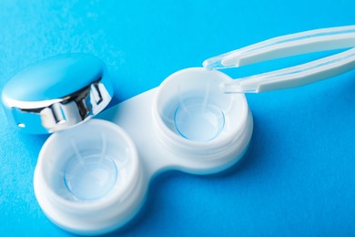Photo of Contact lenses in case and tweezers on blue background, above view