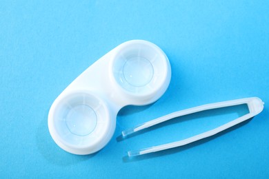 Photo of Contact lenses in case and tweezers on blue background, flat lay
