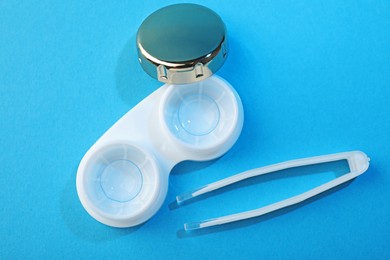 Photo of Contact lenses in case and tweezers on blue background, flat lay
